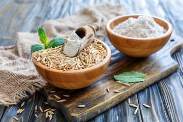 Whole oats and oat flour in bowl on old table with burlap, selective focus.