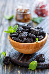 Dried prunes in a bowl on wooden table, selective focus.