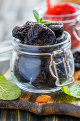 Dried black plum in glass jar on wooden table, selective focus.