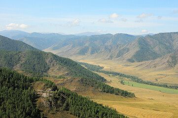 Naklejka premium The gentle slopes of high hills overgrown with coniferous forests smoothly descend into the picturesque valley on a sunny autumn day.