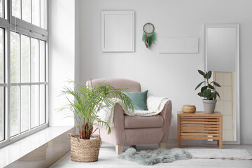 Interior of modern living room with armchair, plants and dream catcher hanging on light wall