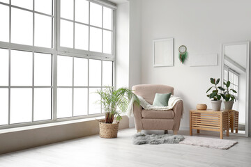 Interior of modern living room with armchair, plants and dream catcher hanging on light wall