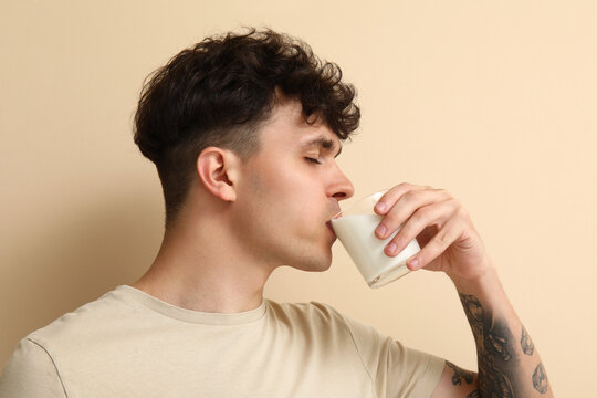 Young man drinking milk on beige background, closeup