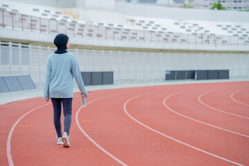 Fototapeta premium A young asian Muslim woman wearing a black hijab is exercising and running at an outdoor stadium in the morning. Modern Muslim woman concept, Muslim woman sport concept, Islam