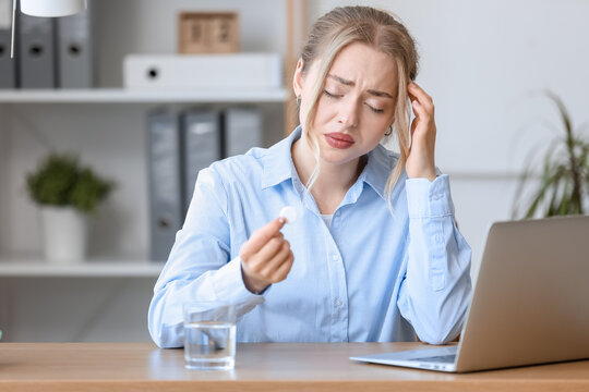 Young businesswoman with soluble tablet suffering from headache in office