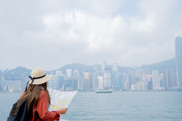 Asian tourist, cute woman with long hair are traveling in Hong Kong along with map and her camera with fun on her holiday,traveler relaxing and enjoying at Victoria harbour in Hong Kong.