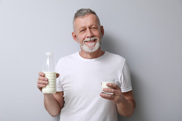 Mature man with bottle and glass of milk on light background