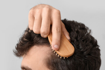 Naklejka premium Young brunette man brushing hair on light background, closeup