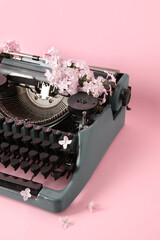 Vintage typewriter with lilac flowers on pink background, closeup