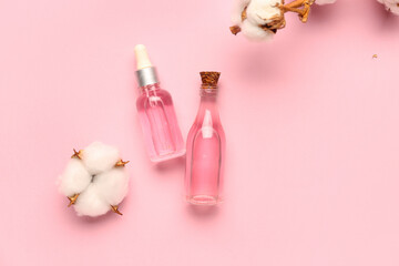 Bottles of cosmetic products and cotton flowers on pink background
