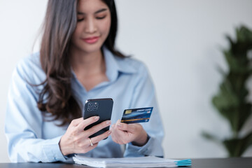 Close up Asian woman with smart phone and credit card, she fills in credit card information to pay for goods and services, online shopping concept pay by credit card via smartphone.