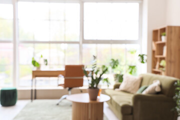 Interior of stylish living room with cozy green sofa and comfortable workplace near big window, blurred view
