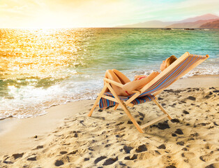 Fototapeta na wymiar Girl tans on a deck chair on a beautiful beach during sunset