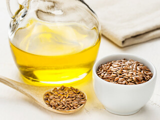Brown flax seeds in spoon and flaxseed oil in glass bottle on trendy textured white concrete...