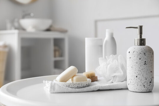 Soap dispenser, bars, towel and shower sponge on white table in bathroom, closeup