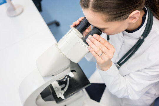 Doctor or biologist with stethoscope scrutinizing tissue under microscope