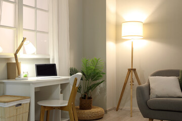 Interior of living room with cozy grey sofa, comfortable workplace and glowing lamp