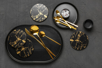 Clean plates, drink coasters and golden cutlery on black grunge table