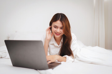 Happy smiling asian woman stretching on bed in the morning and using laptop computer