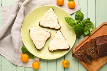 Plate of tasty sandwiches with cream cheese and tomatoes on green wooden background