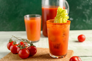 Glasses and jug of bloody mary with celery on green wooden table