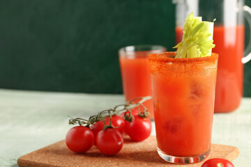 Glasses and jug of bloody mary with celery on green wooden table