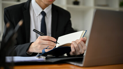 Cropped image of a professional Asian male lawyer writing something on his notebook