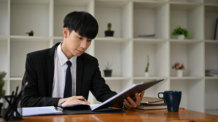 A professional Asian male lawyer is writing a notice letter at his desk in the office.