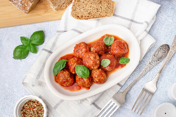 Plate of tasty meat balls with tomato sauce and basil on grey table