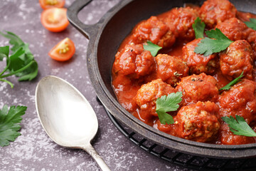 Frying pan of tasty meat balls with tomato sauce and parsley on grey background