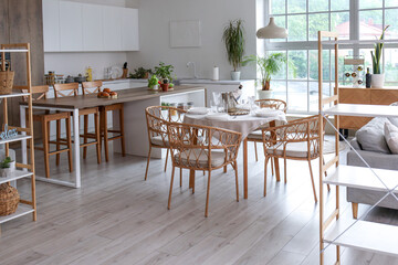 Interior of light open space kitchen with served dining table, island and big window