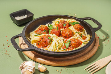 Frying pan of boiled pasta with tomato sauce and meat balls on green background