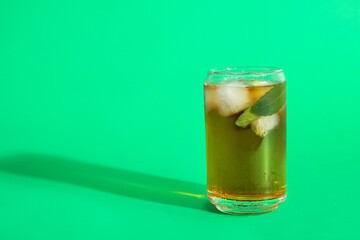 Glass of ice tea with mint on green background