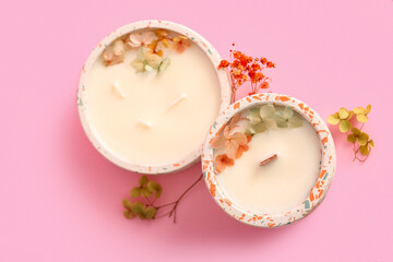 Holders with candles and flowers on pink background