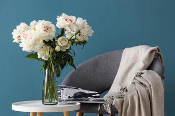 Vase of white peonies with coffee table, chair and magazine near blue wall © Pixel-Shot