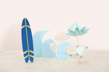 Creative composition with mini surfboard, miniature deckchair and paper waves on white table