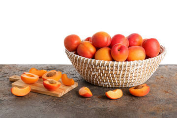 Wicker basket with ripe apricots on table against white background