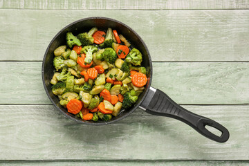 Frying pan with tasty vegetables on green wooden background