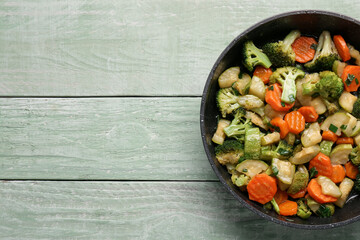 Frying pan with tasty vegetables on green wooden background