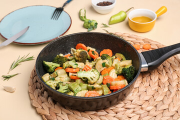 Frying pan with tasty vegetables on yellow background