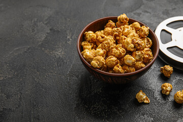 Bowl with tasty popcorn and film reel on black background