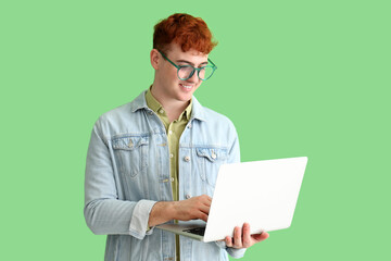 Young redhead man using laptop on green background