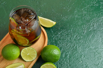 Glass of cold Cuba Libre cocktail on green background