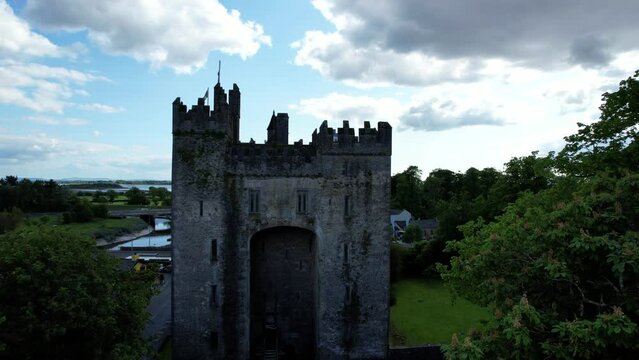 Bunratty Castle among Folk Park trees in Ireland, Atlantic Ocean in background. Aerial ascending