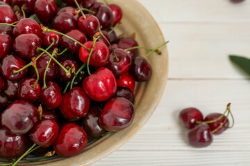 Bowl with sweet cherries on white wooden background
