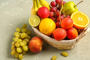 Wicker basket with different fresh fruits on grey background