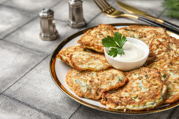 Plate of tasty zucchini fritters with sour cream on grey tile background