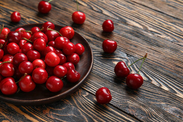 Plate with sweet cherries on wooden background