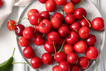Plate with sweet cherries on white background