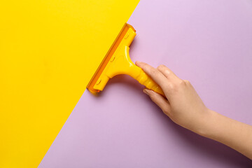 Female hand holding squeegee on lilac and orange background